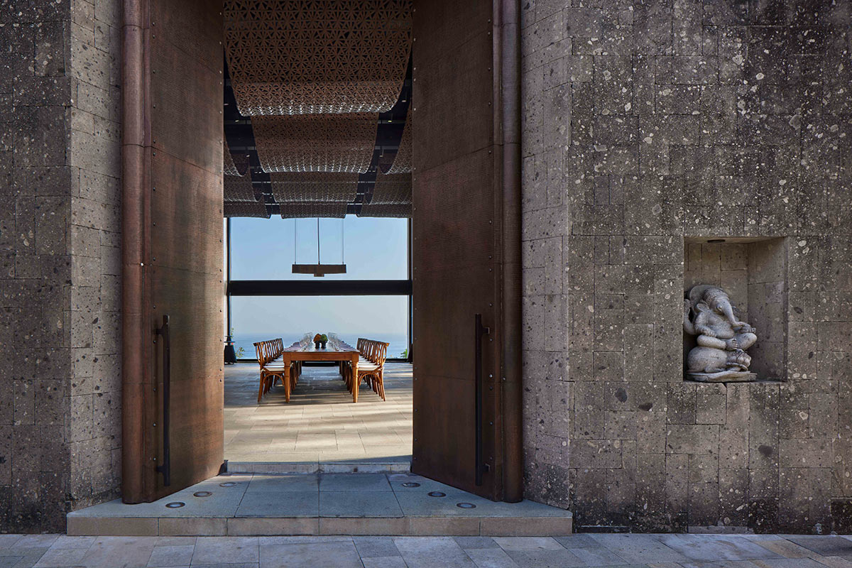 Tall bronze doors opening onto a stone terrace dining table above the sea